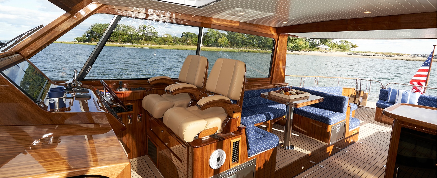 Daychaser cockpit with teak wood helm station, tan leather captain's chairs, and blue upholstered seating overlooking calm coastal waters
