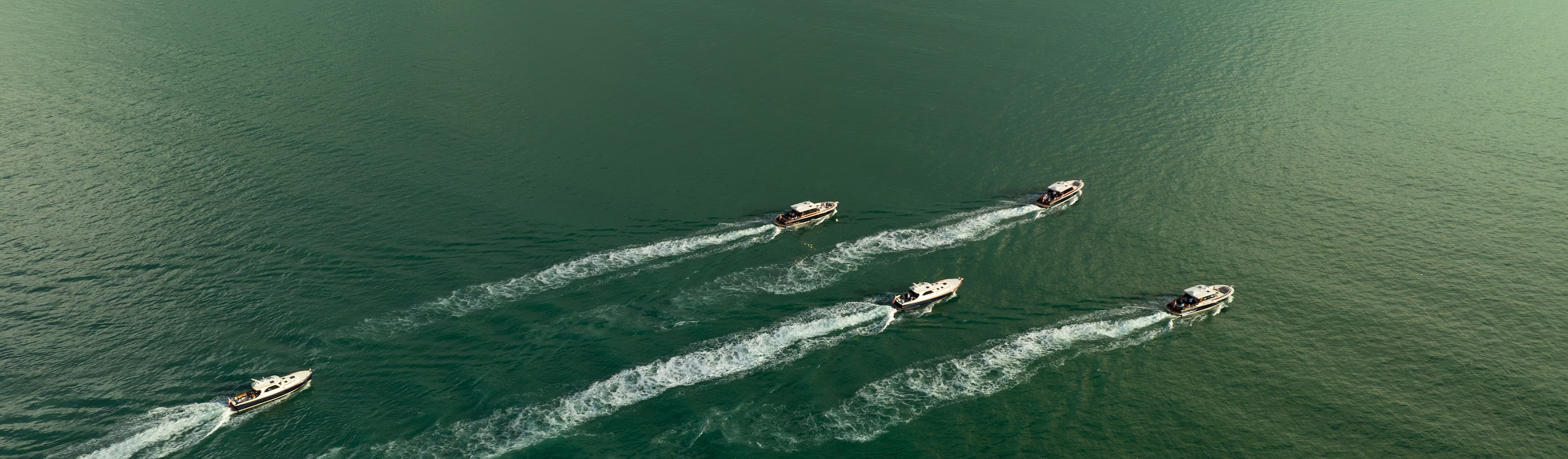 Aerial shot of a fleet of daychasers cruising through the aqua green water.